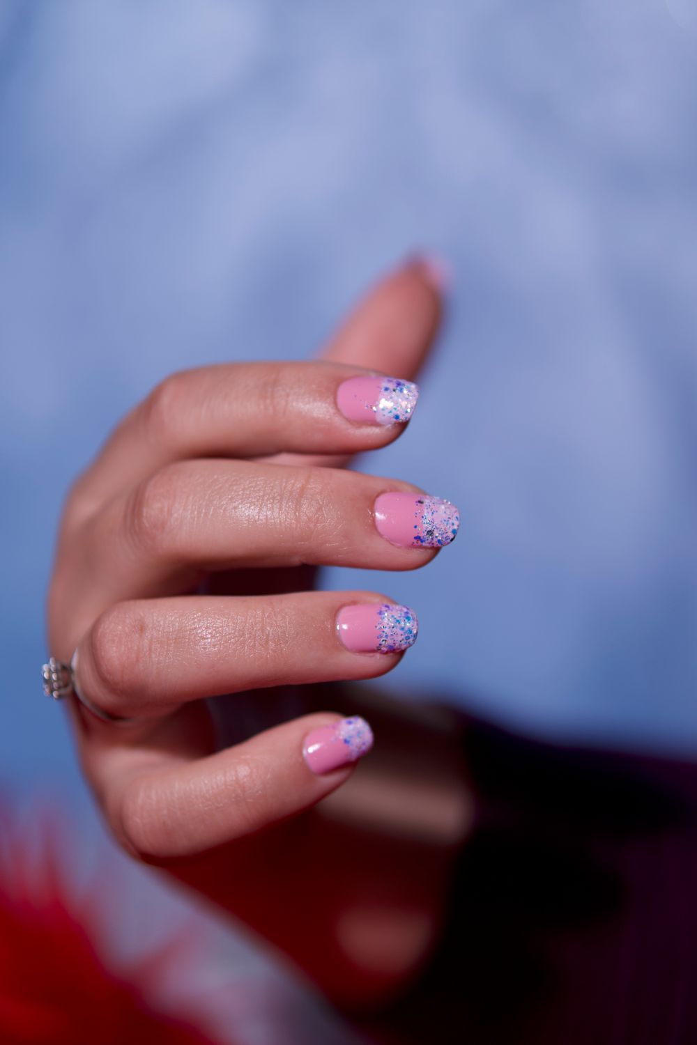 Hand met zachtroze nagels met lila glitterpunten tegen een blauwe achtergrond