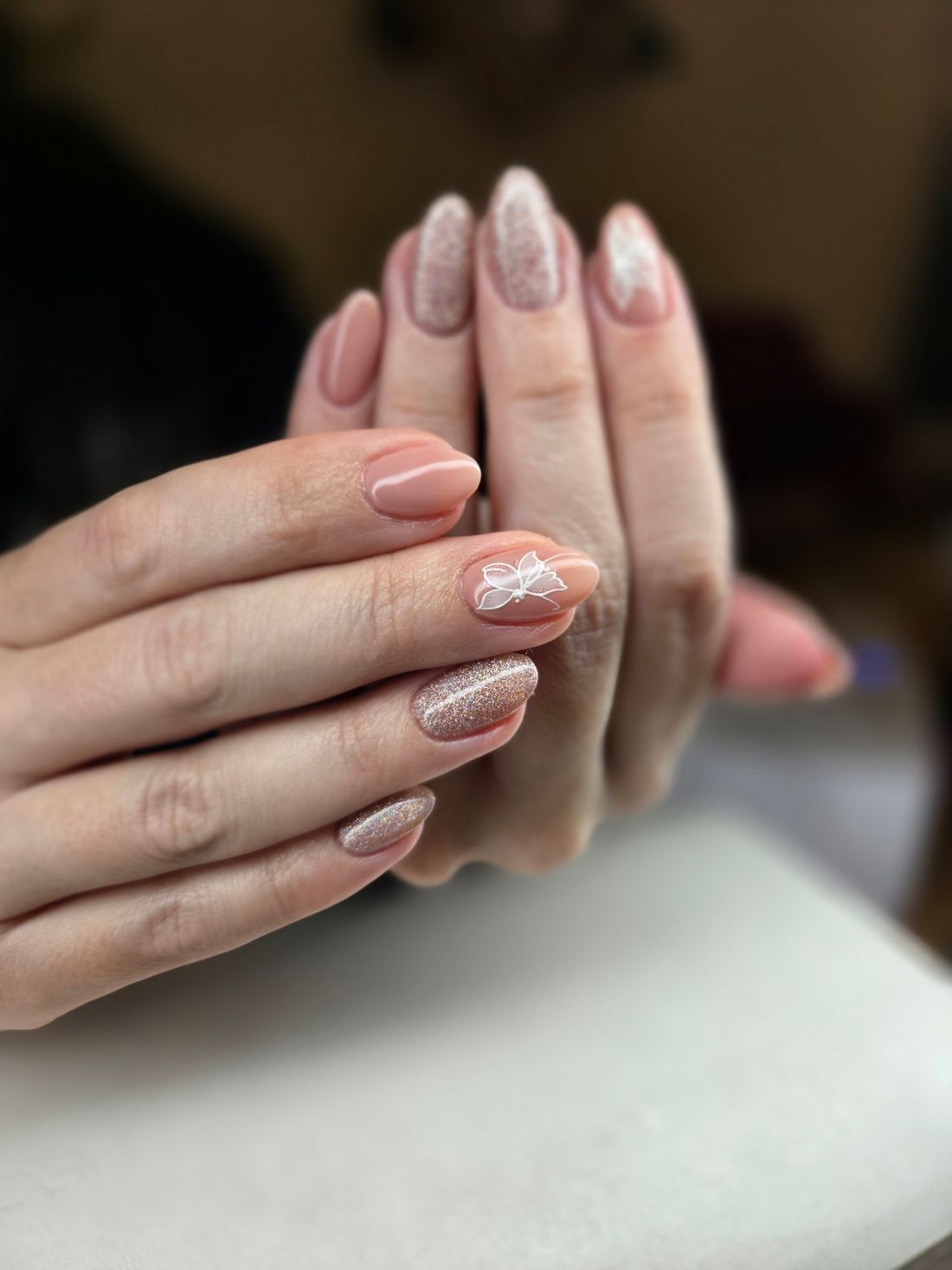 Handen met nude nagels, een deel met fijne glitter en een klein bloemmotief