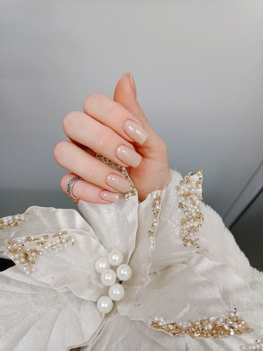 Hand met nude nagels boven een witte sierbloem met parels