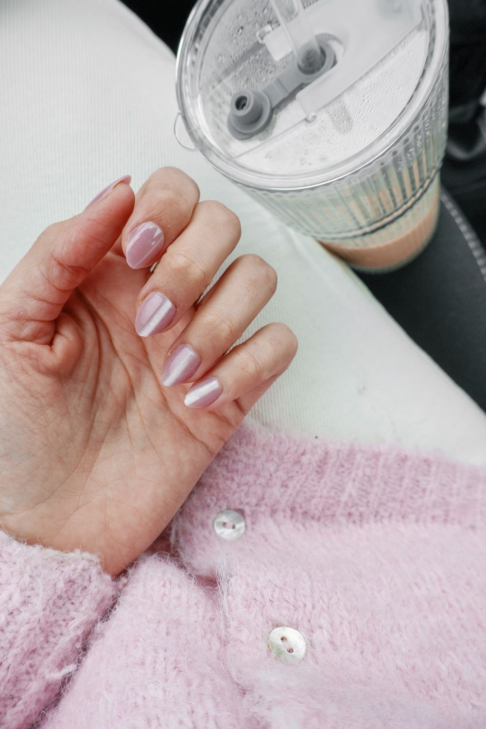 Hand met glanzende pastelroze nagels boven een roze gebreid vest