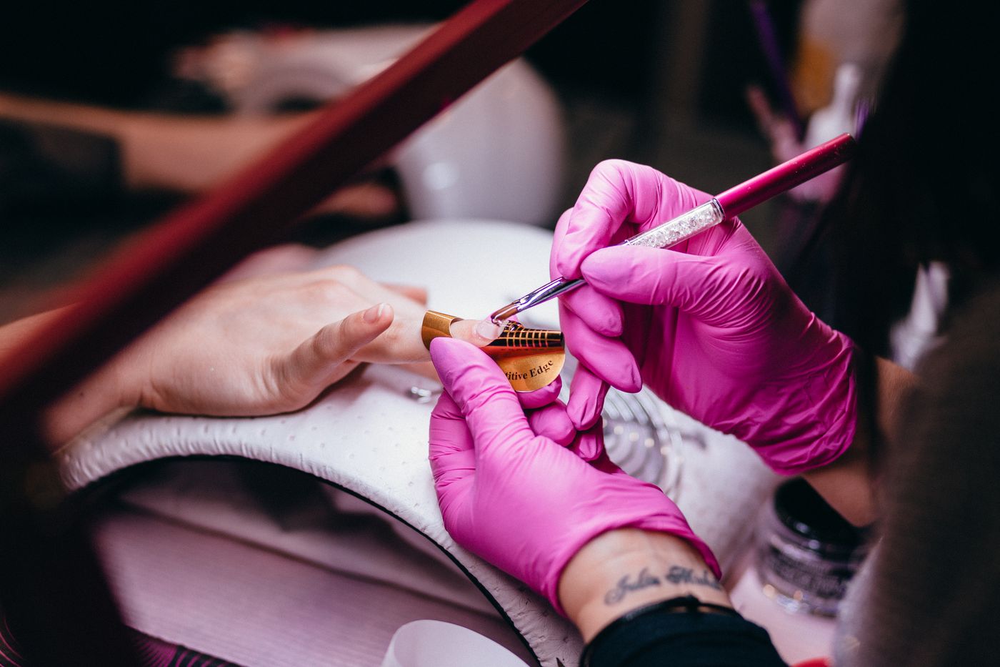 Een nagelstyliste met roze handschoenen brengt met een fijn penseel een ontwerp aan op een nagel
