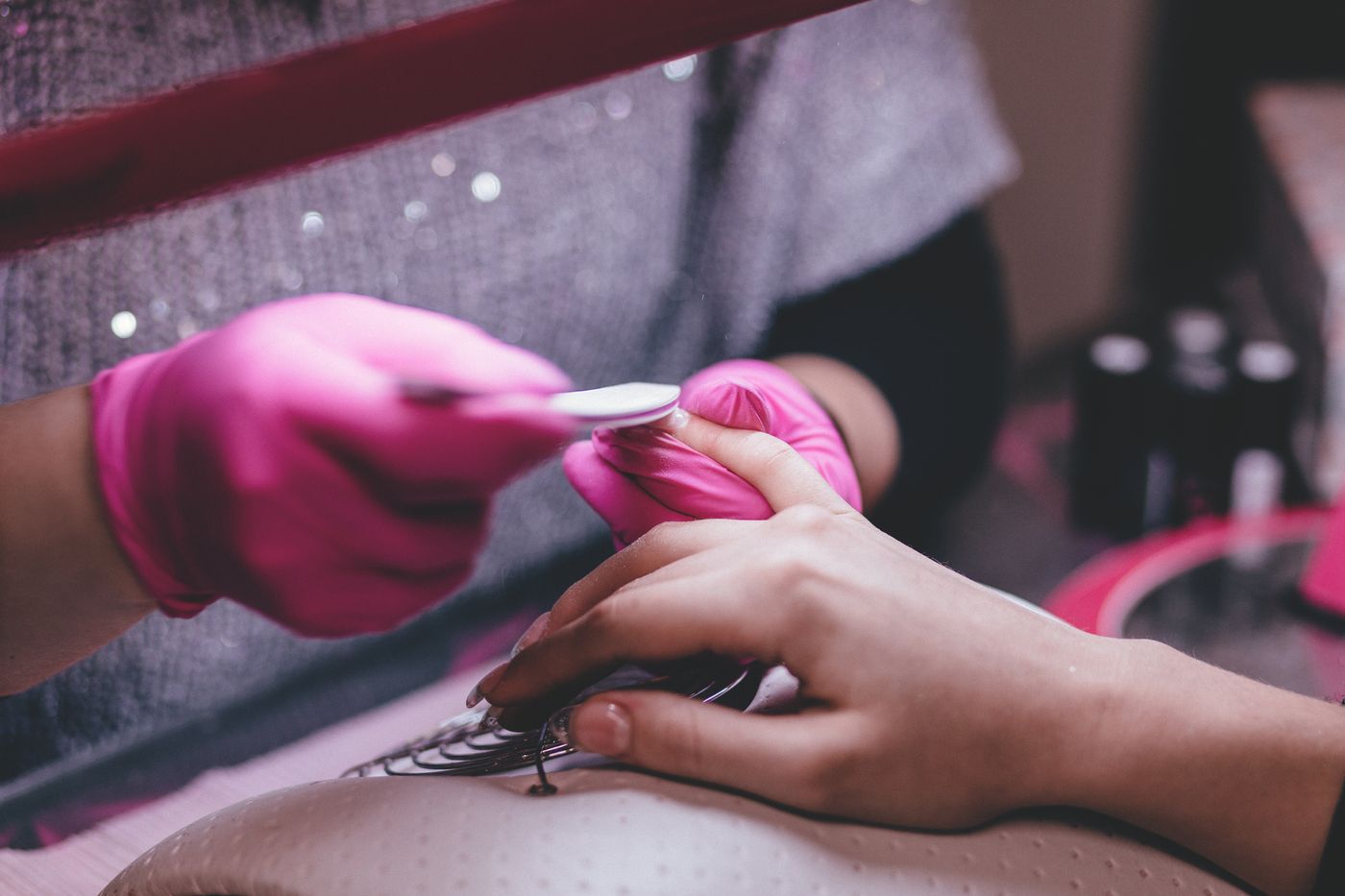 Een nagelstyliste met roze handschoenen vijlt de nagels van een klant